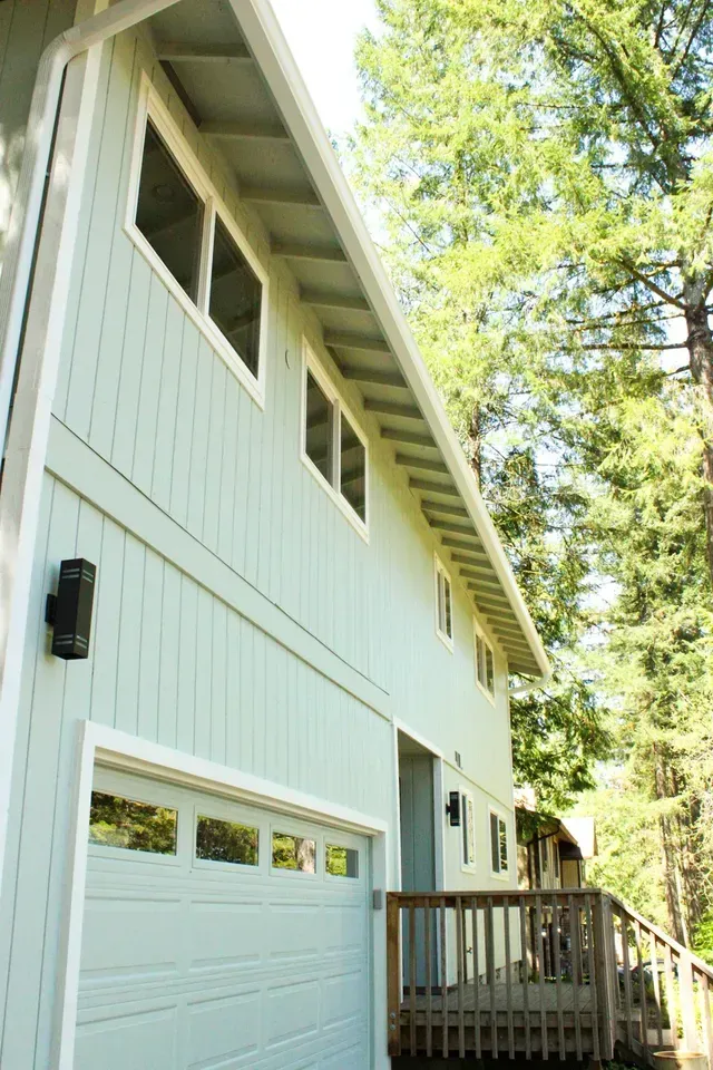 White two-story house with garage and wooden deck, viewed from below among trees