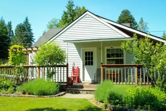 White house with front porch and red chair surrounded by lush green garden