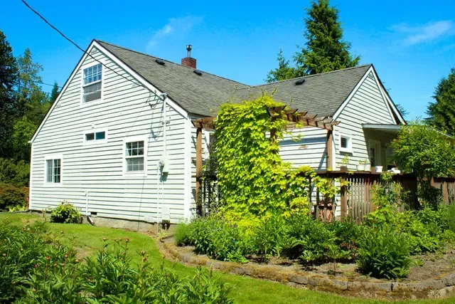 White farmhouse with ivy-covered porch and green garden under a blue sky