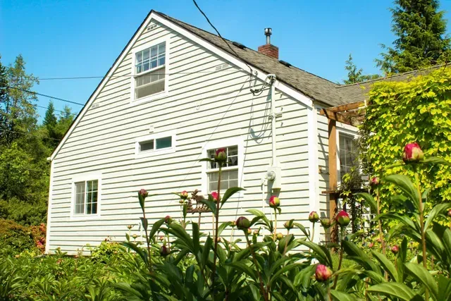 White farmhouse with sloped roof and garden flowers under a blue sky