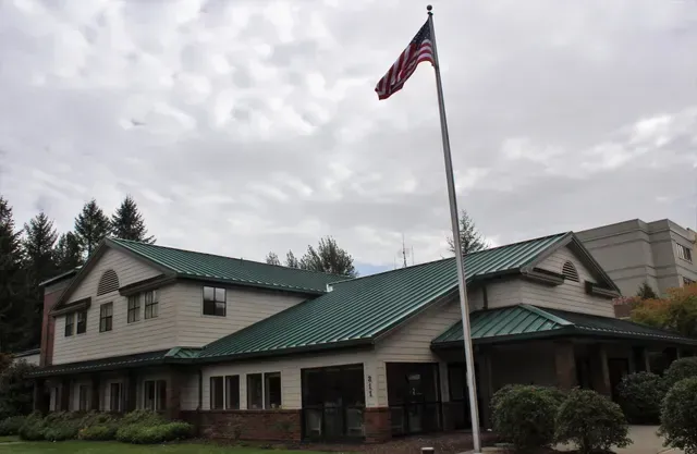 Large lodge-style building with a green roof and a U.S. flag on a cloudy day