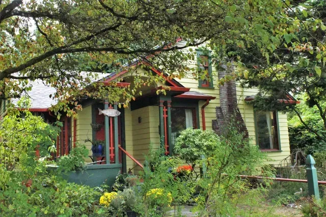 Small green house with red trim nestled in lush garden foliage