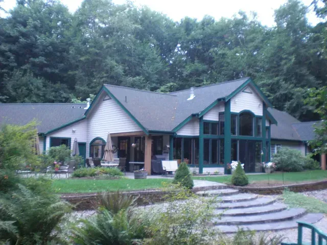 Large house with green roof and stone steps, surrounded by lush trees and landscaping.