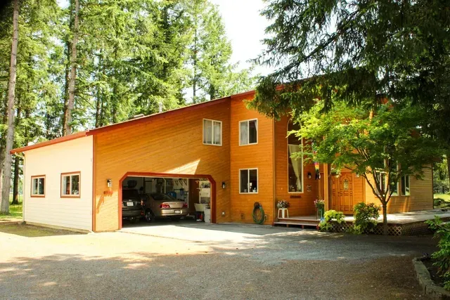 Orange house with open garage surrounded by tall trees and a gravel driveway