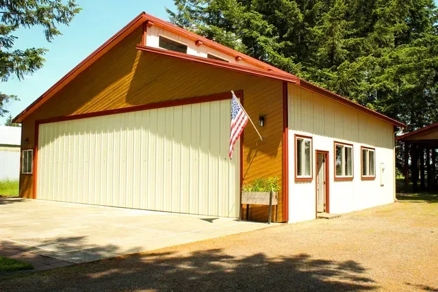 Small cream-and-red garage or workshop building with an American flag hanging by the entrance.