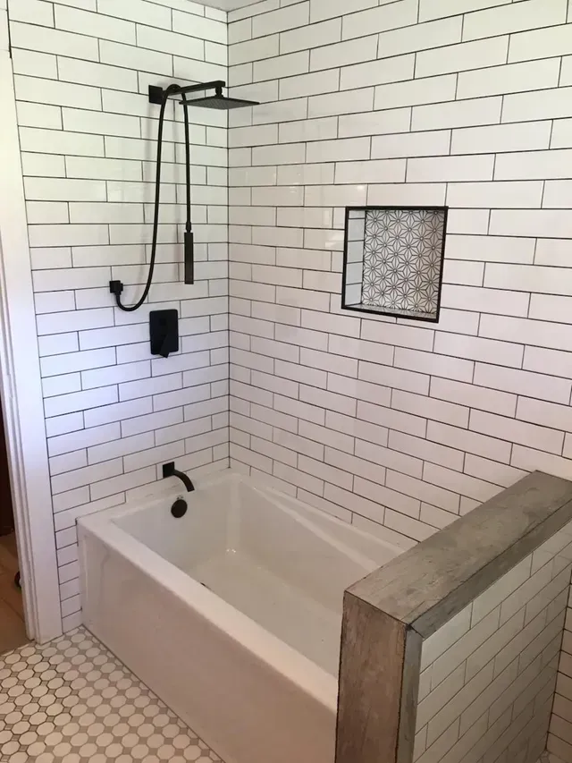White tiled bathroom with a bathtub, shower head, and small window inset in the wall