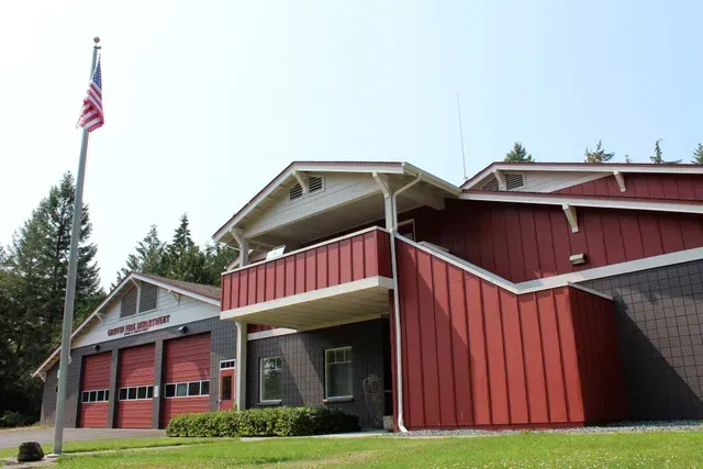 Red fire station with American flag and open garage doors on a grassy lot