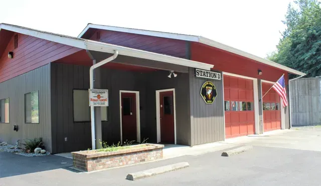 Small brown building with red garage doors, white trim, and an American flag outside.
