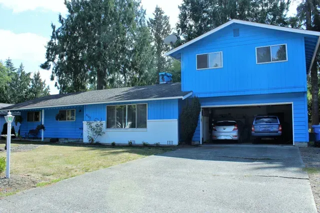 Blue two-story house with attached garage and driveway, surrounded by trees.