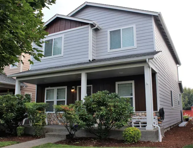 Two-story gray house with white trim, front porch, and shrubs in front yard