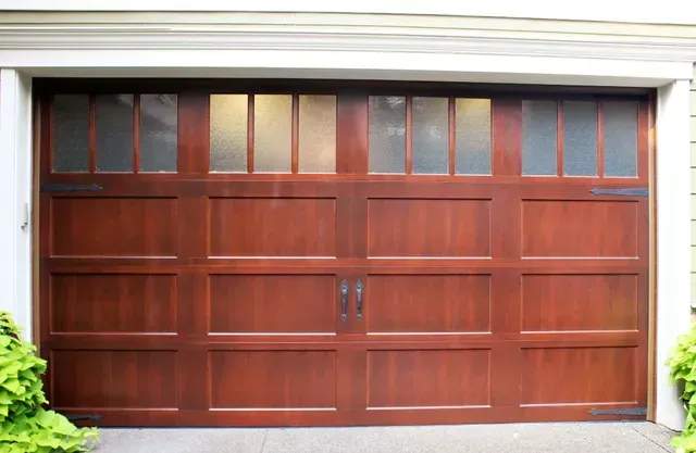 Wooden garage door with small upper windows and decorative black handle on a house exterior