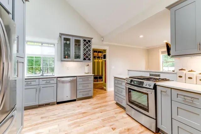 Bright modern kitchen with gray cabinets, white walls, wood floors, and stainless steel appliances