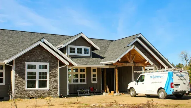 New house under construction with dark siding and a white work van parked in front