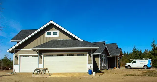New suburban house with gray siding, three-car garage, and a white pickup truck under a clear blue sky
