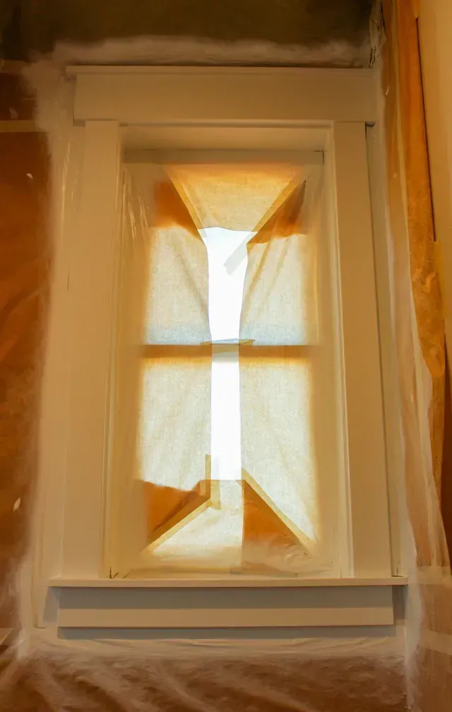 Backlit window with sheer curtains in a beige wall, sunlight streaming through.