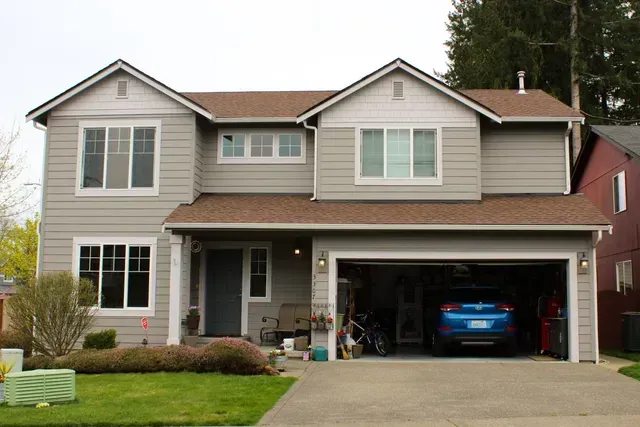 Suburban two-story house with a blue car in the open garage and a front lawn