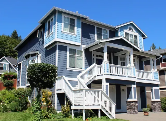 Blue and white multi-story house with porch and stairs on a sunny hillside