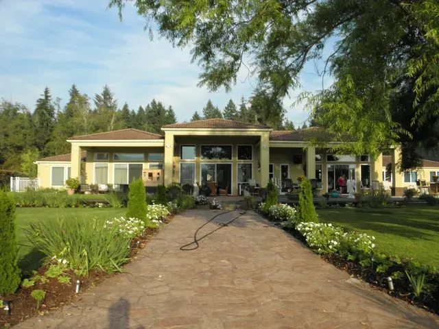 Modern house with a long stone walkway, lush garden, and trees under a bright sky