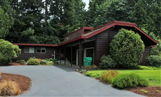 Dark wood house with red trim beside a curved driveway and lush trees.