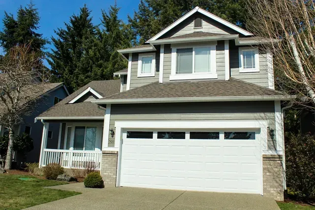 Suburban two-story house with white garage door, front porch, and beige siding in daylight