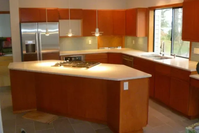 Modern kitchen with warm wood cabinets, stainless steel appliances, and a large island with beige countertops