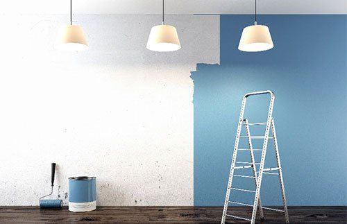 Wall partially painted white and blue, with a ladder, paint can, and lights.
