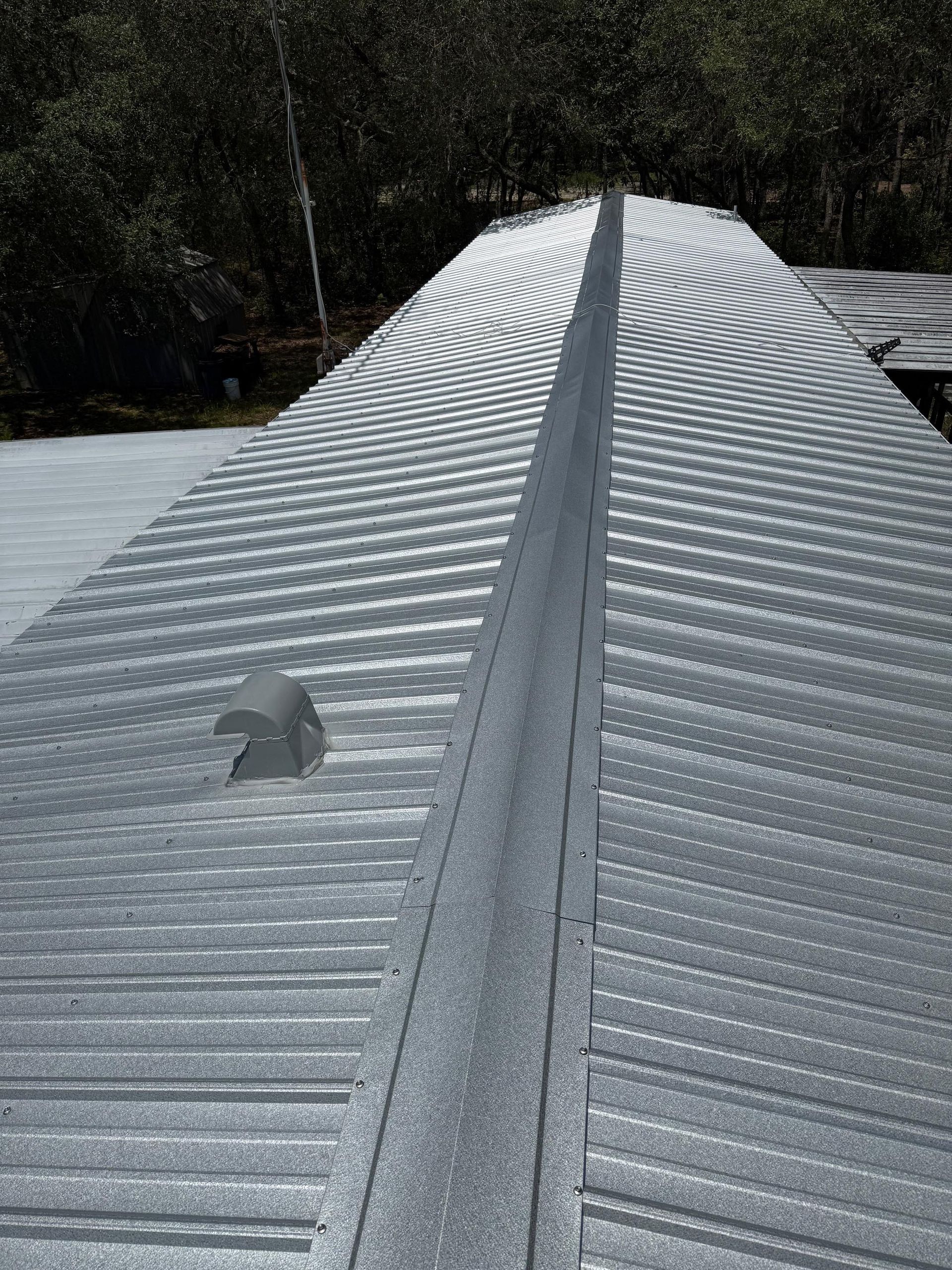 An elevated view of a metal roof on a mobile home with a center ridge cap and a small vent.