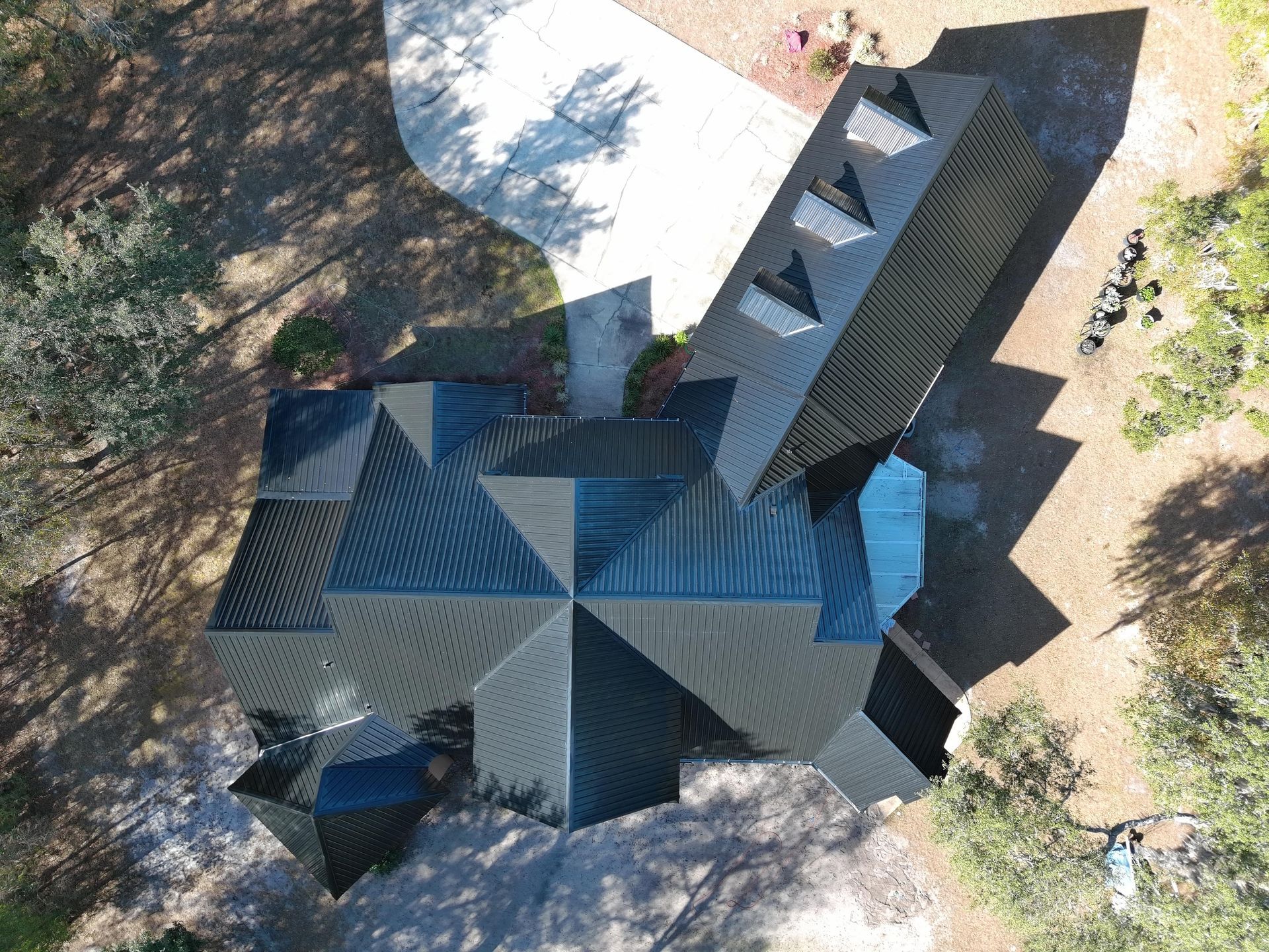 A top-down aerial view of a dark metal roof on a residential home with multiple gables and a detached garage.