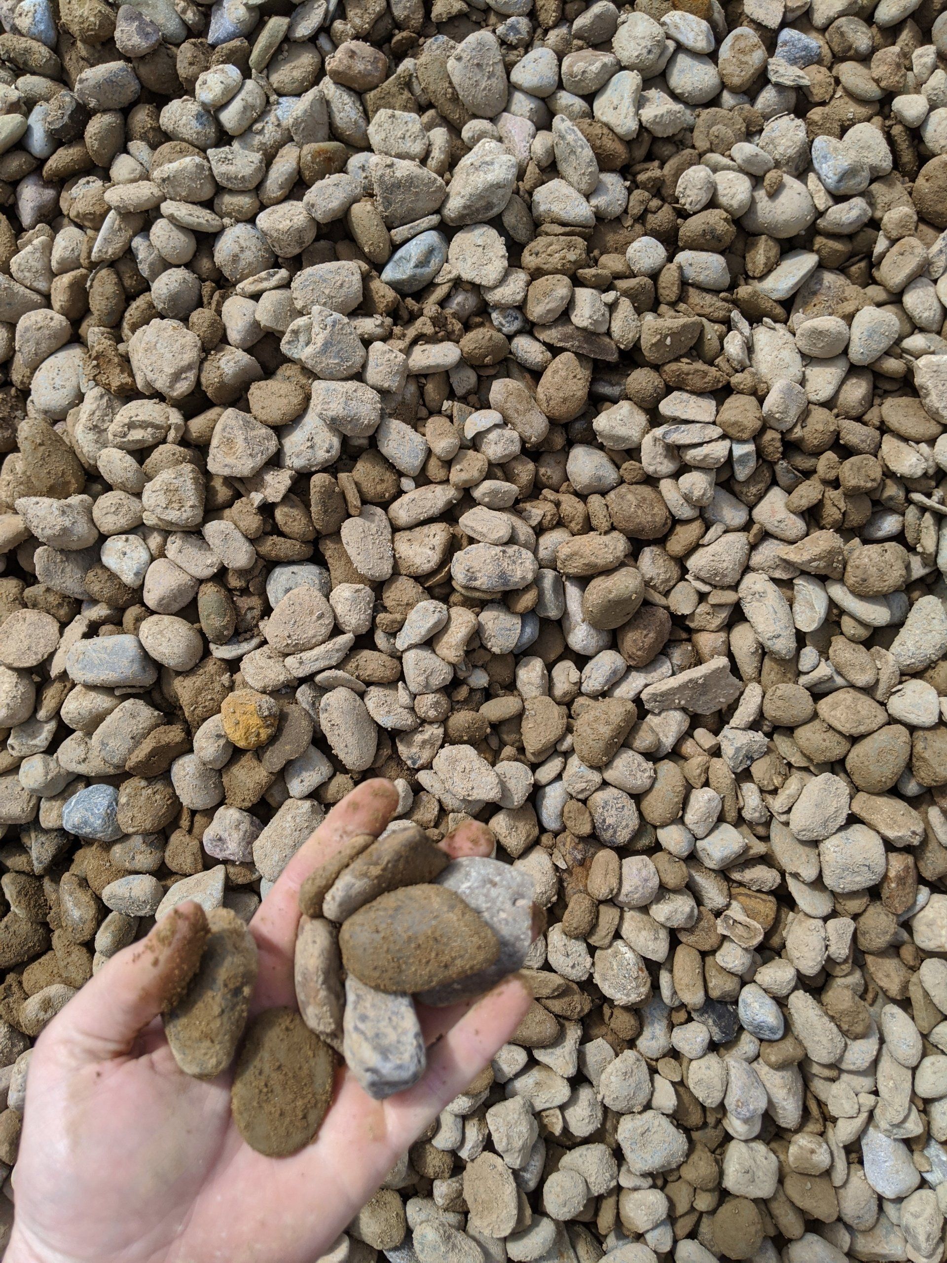 Handful of gray and brown river rock, surrounded by a pile of similar rocks.