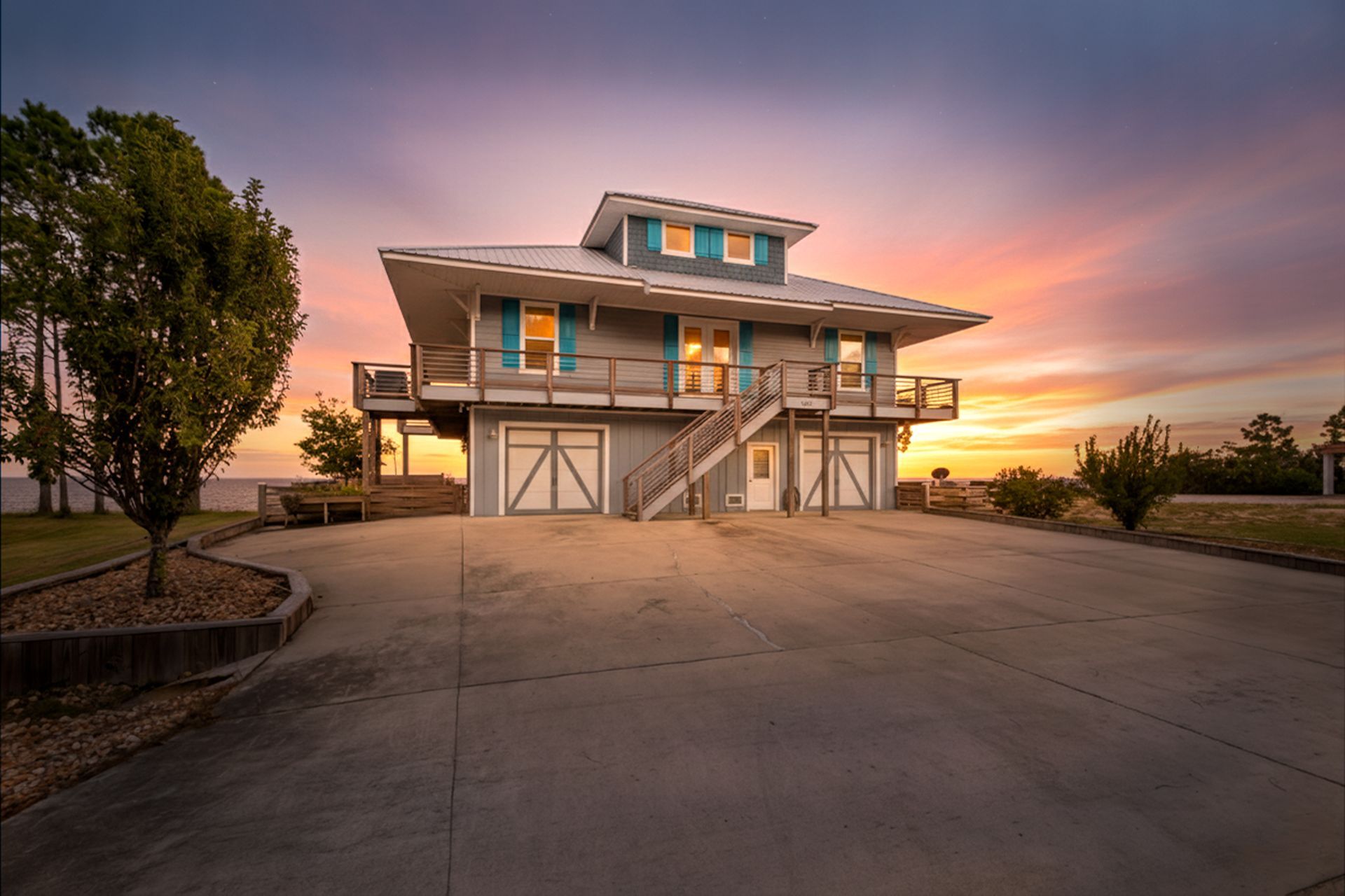 Modern two-story house with a large driveway at sunset, with warm pink-orange sky.
