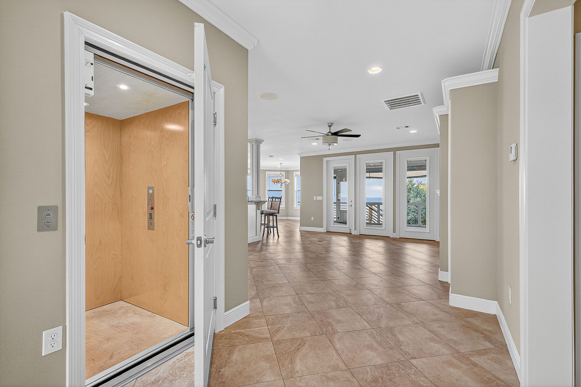 Bright modern hallway with beige tile floors, open elevator on left, and large windows at the end.