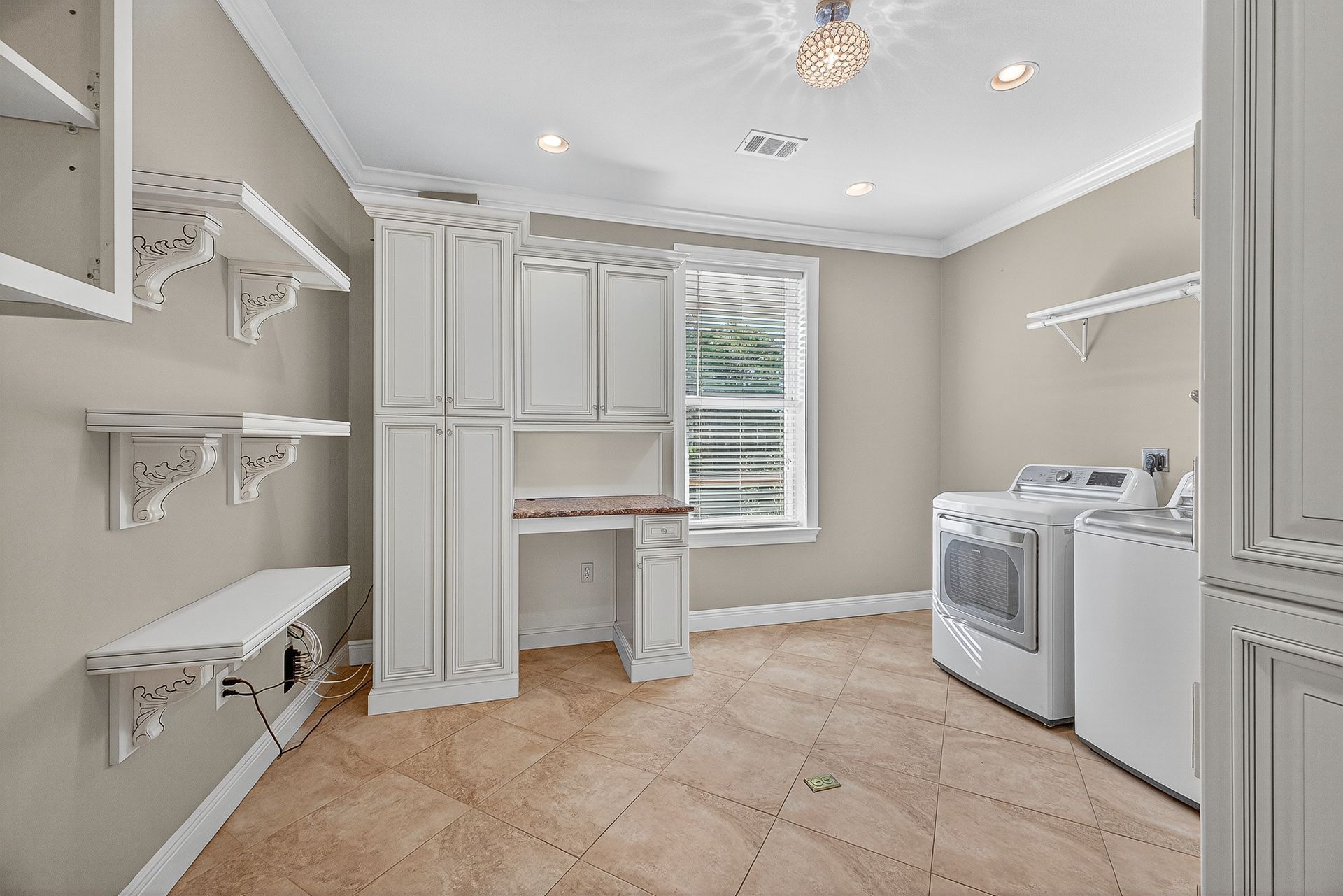 Bright laundry room with white cabinets, shelves, washer and dryer, and tiled floor.