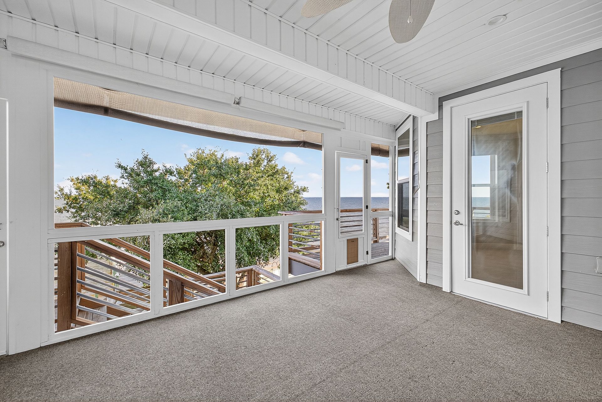 Bright screened porch with gray carpet, white railings, and a view of trees outside
