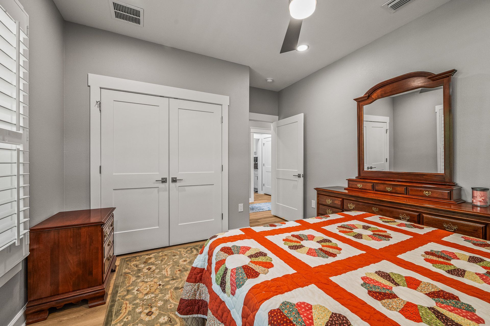 Bedroom with a red-and-white quilt, wooden dresser with mirror, and white closet doors.