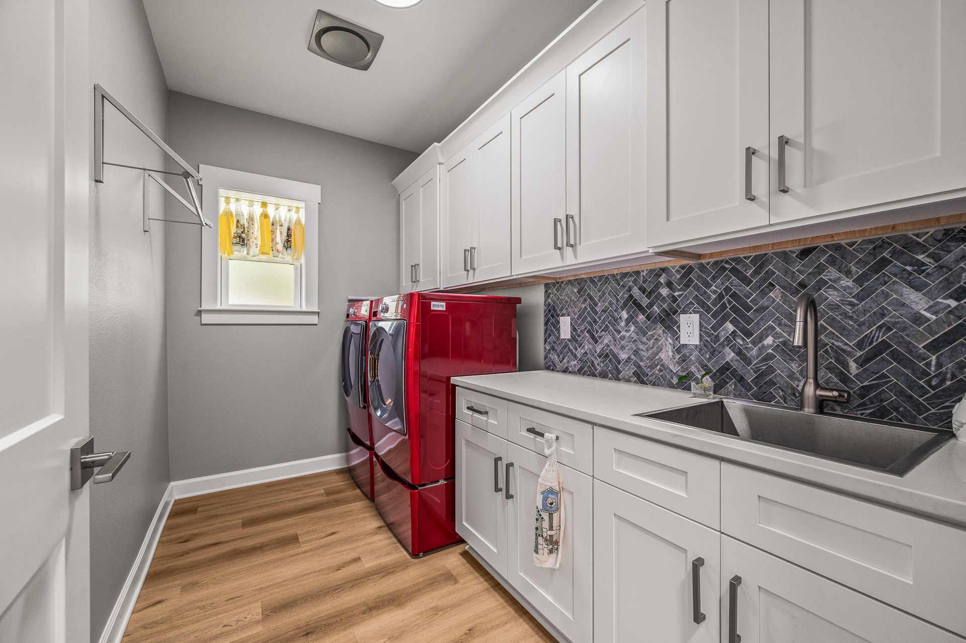 Narrow laundry room with white cabinets, red washer and dryer, gray counters, and wood floor.