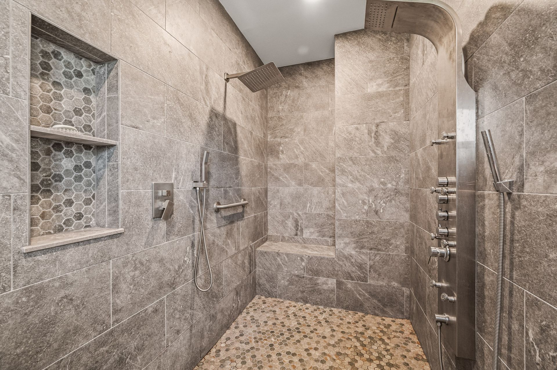 Tiled walk-in shower with bench, glass door, and pebble floor in a modern bathroom