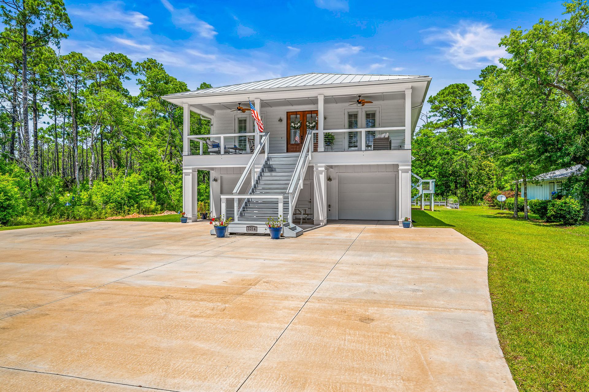 Two-story white house with front stairs and a large concrete driveway under a blue sky