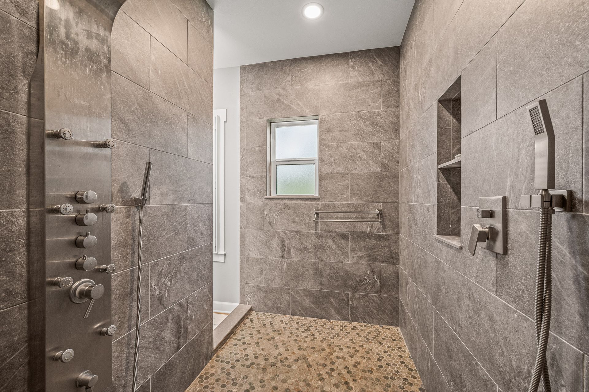 Modern walk-in shower with gray tile walls, pebble floor, glass door, and chrome fixtures