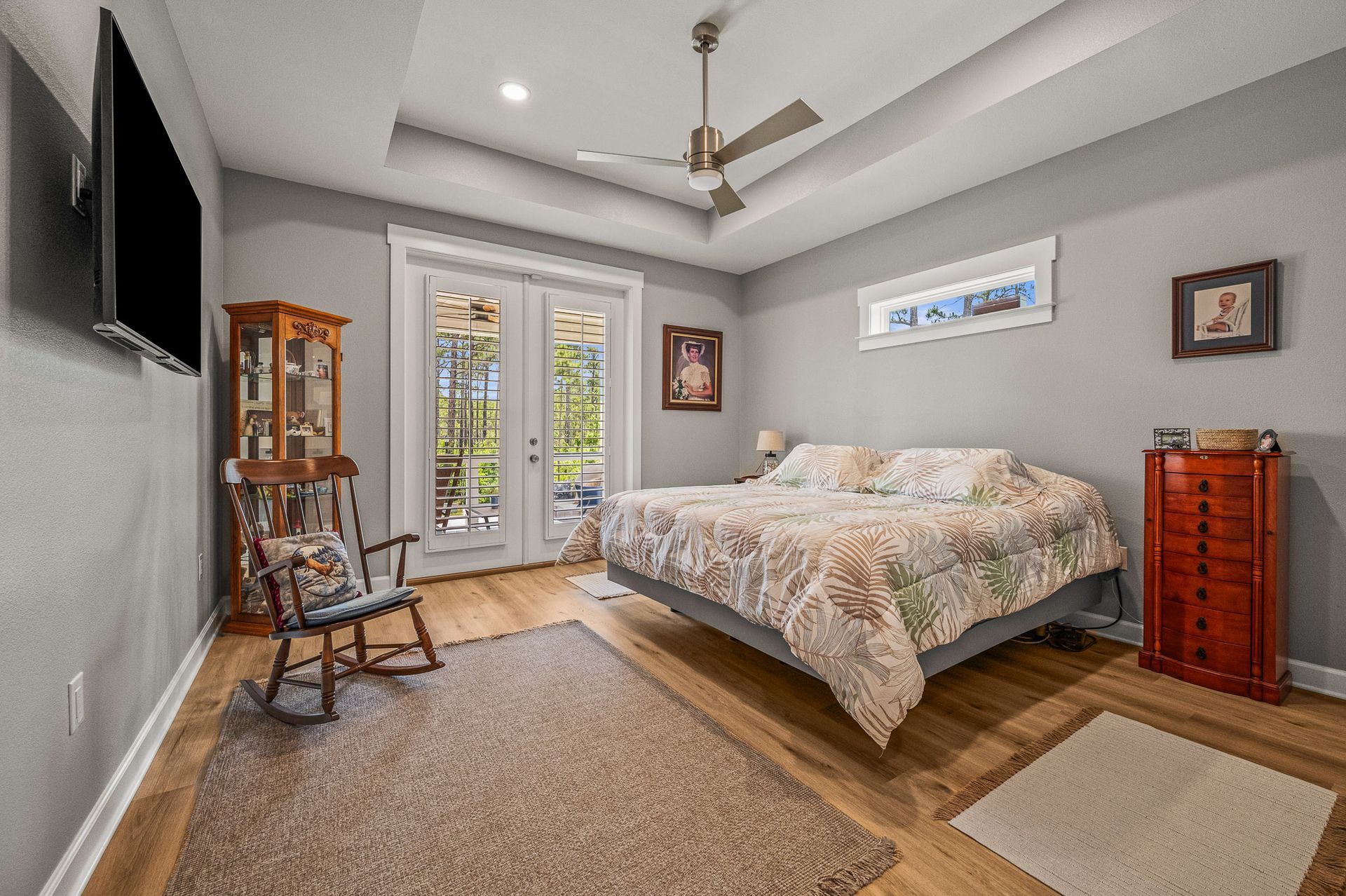 Cozy bedroom with a bed, French doors, TV, rocking chair, and wood dresser in neutral tones.