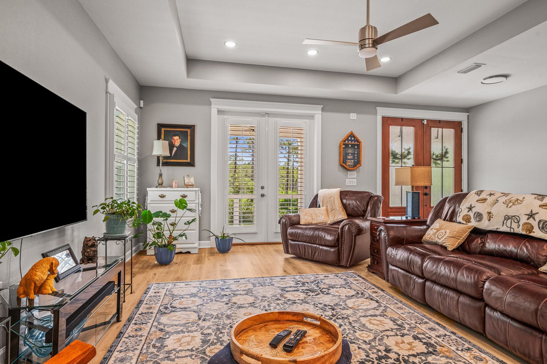 Modern living room with brown leather sofas, patterned rug, ceiling fan, and French doors to a patio.