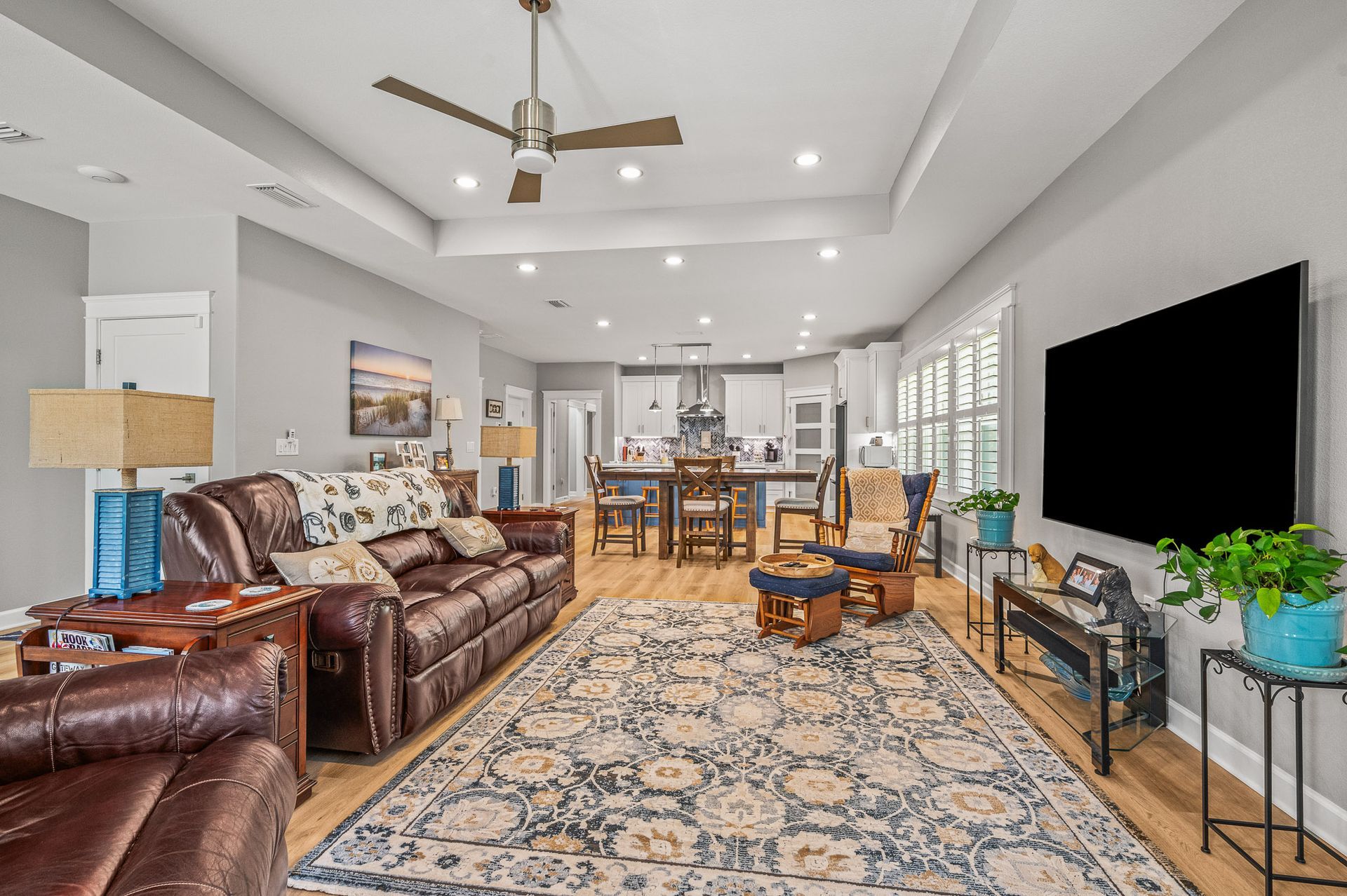 Bright open living room with leather sofas, patterned rug, wall-mounted TV, and dining area beyond