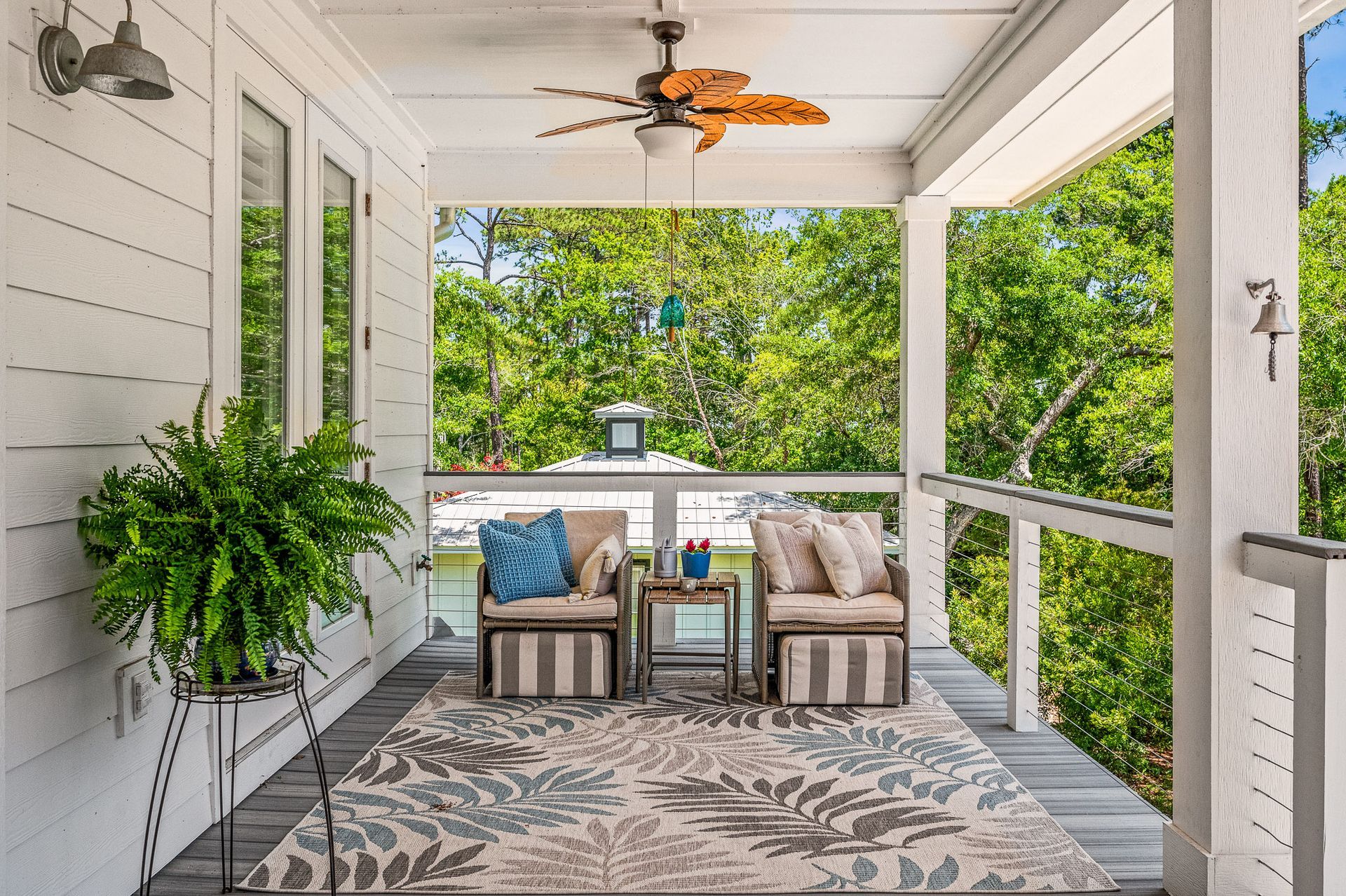 White screened porch with wicker seating, patterned rug, and green garden view