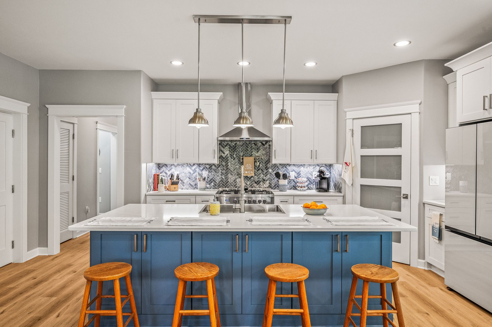 Bright modern kitchen with blue island, white cabinets, stainless appliances, and orange stools