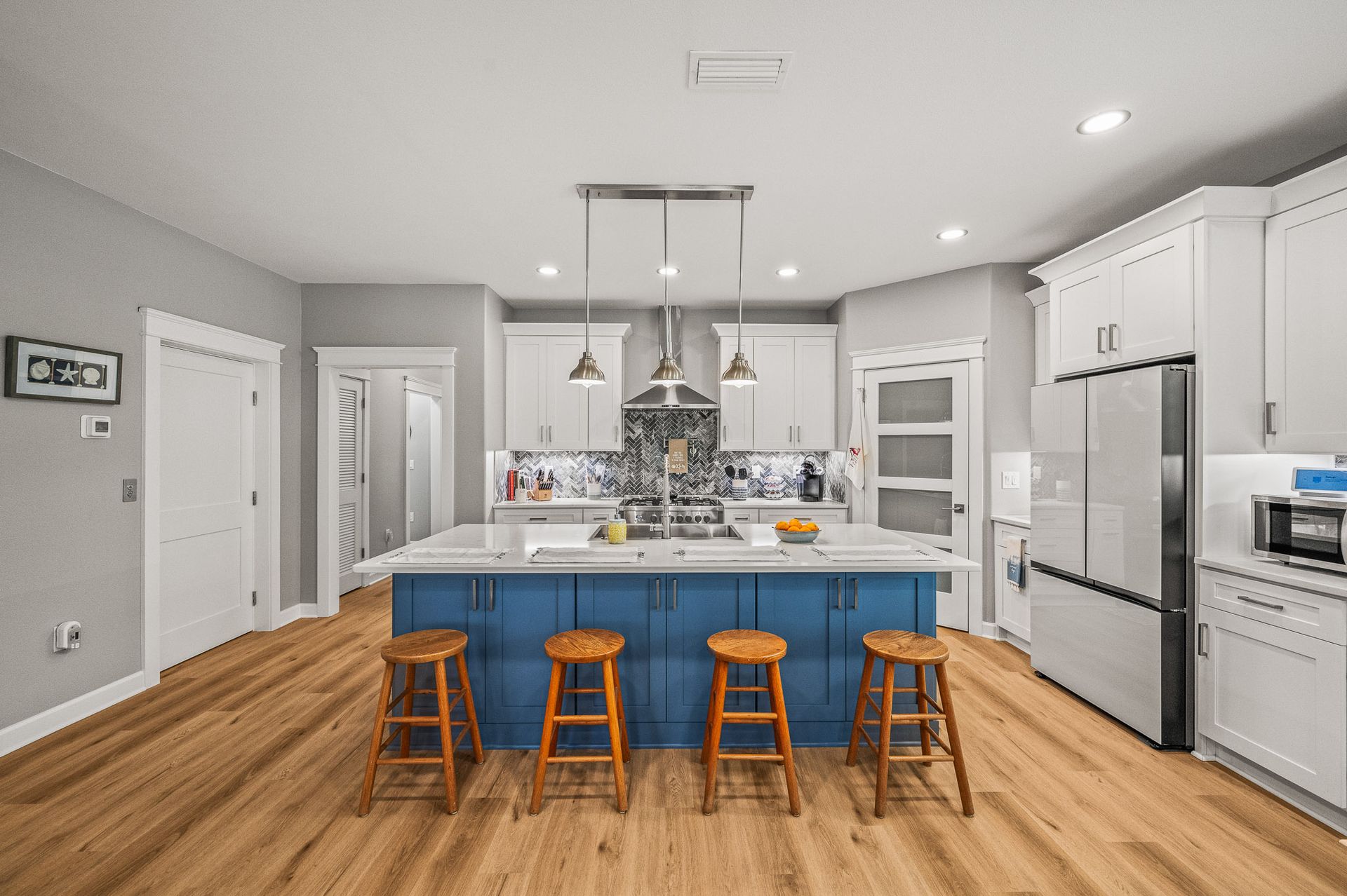 Modern kitchen with blue island, white cabinets, stainless steel appliances, and wooden stools