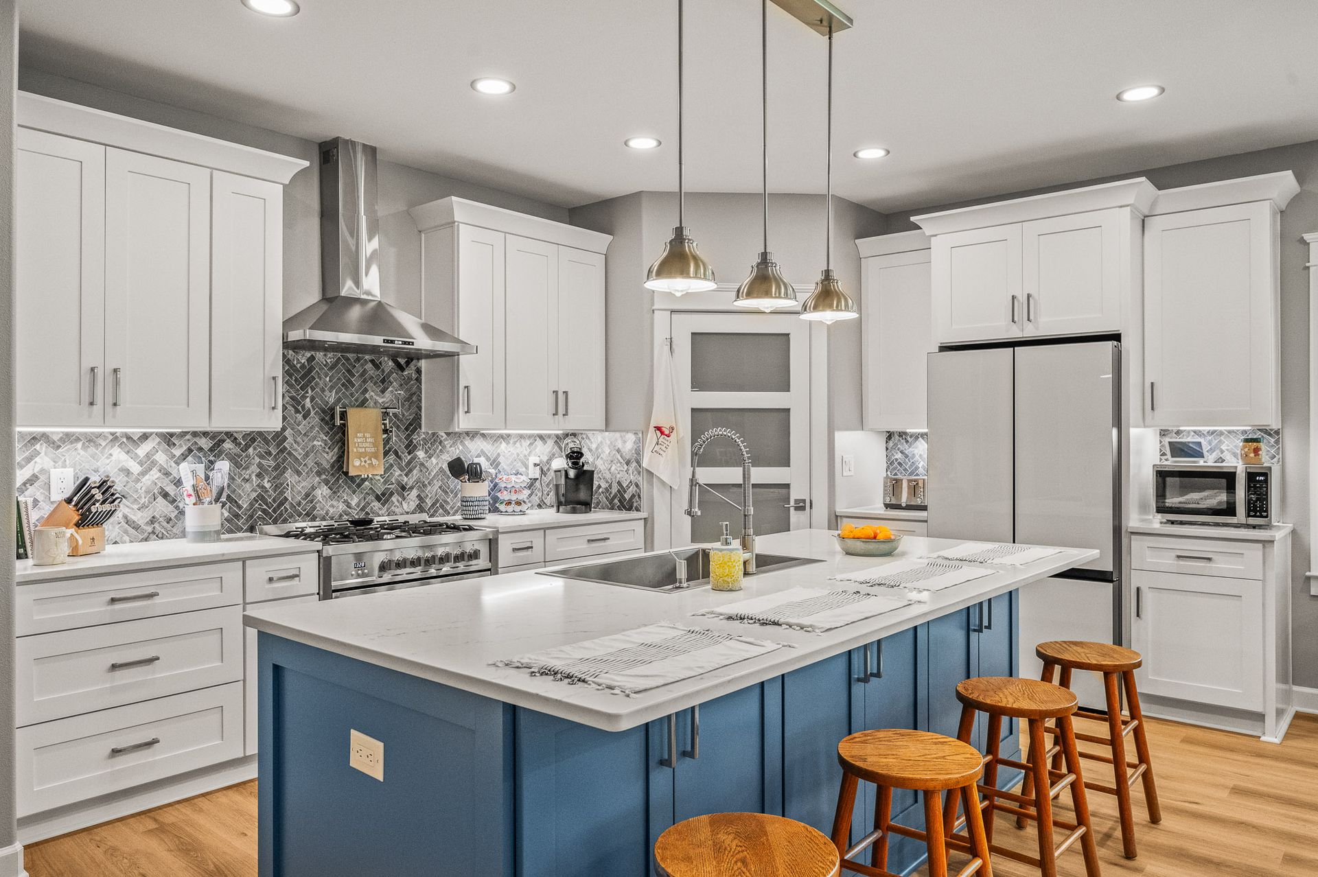 Bright modern kitchen with white cabinets, marble island, blue base, and three wooden stools