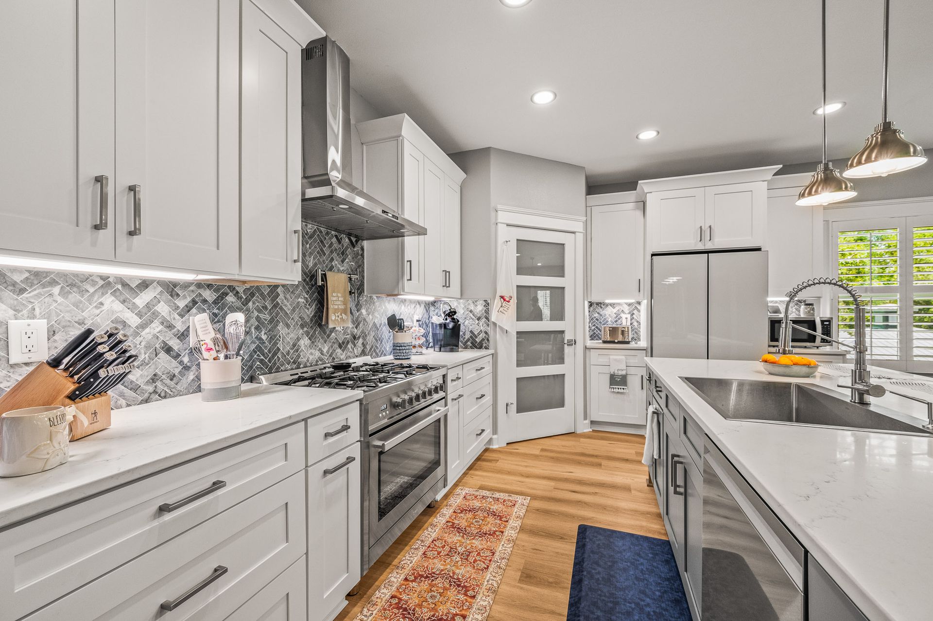 Bright modern white kitchen with marble island, stainless appliances, patterned backsplash, and hardwood floor.