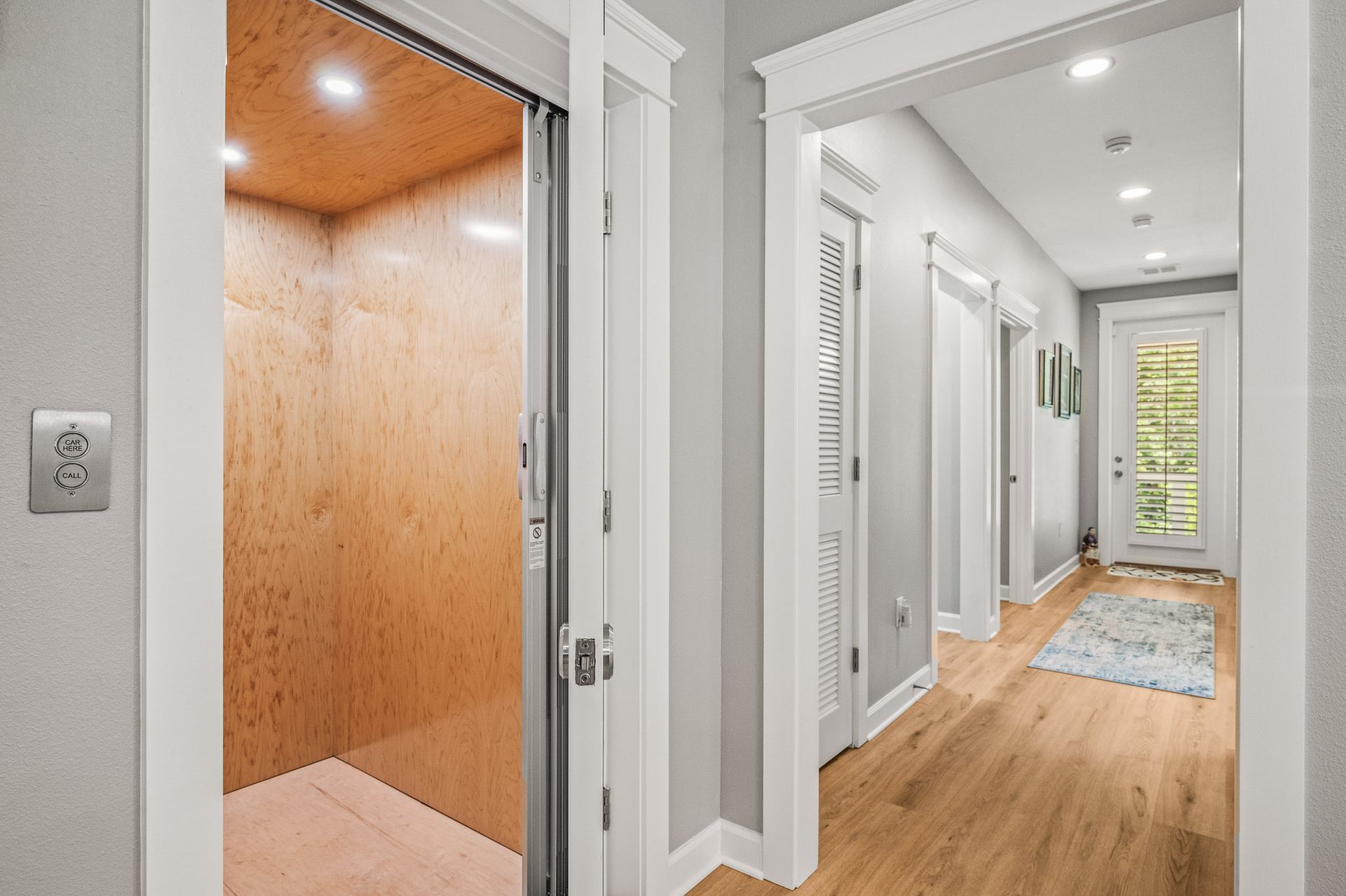 Bright hallway with hardwood floors and an open wood-paneled elevator on the left