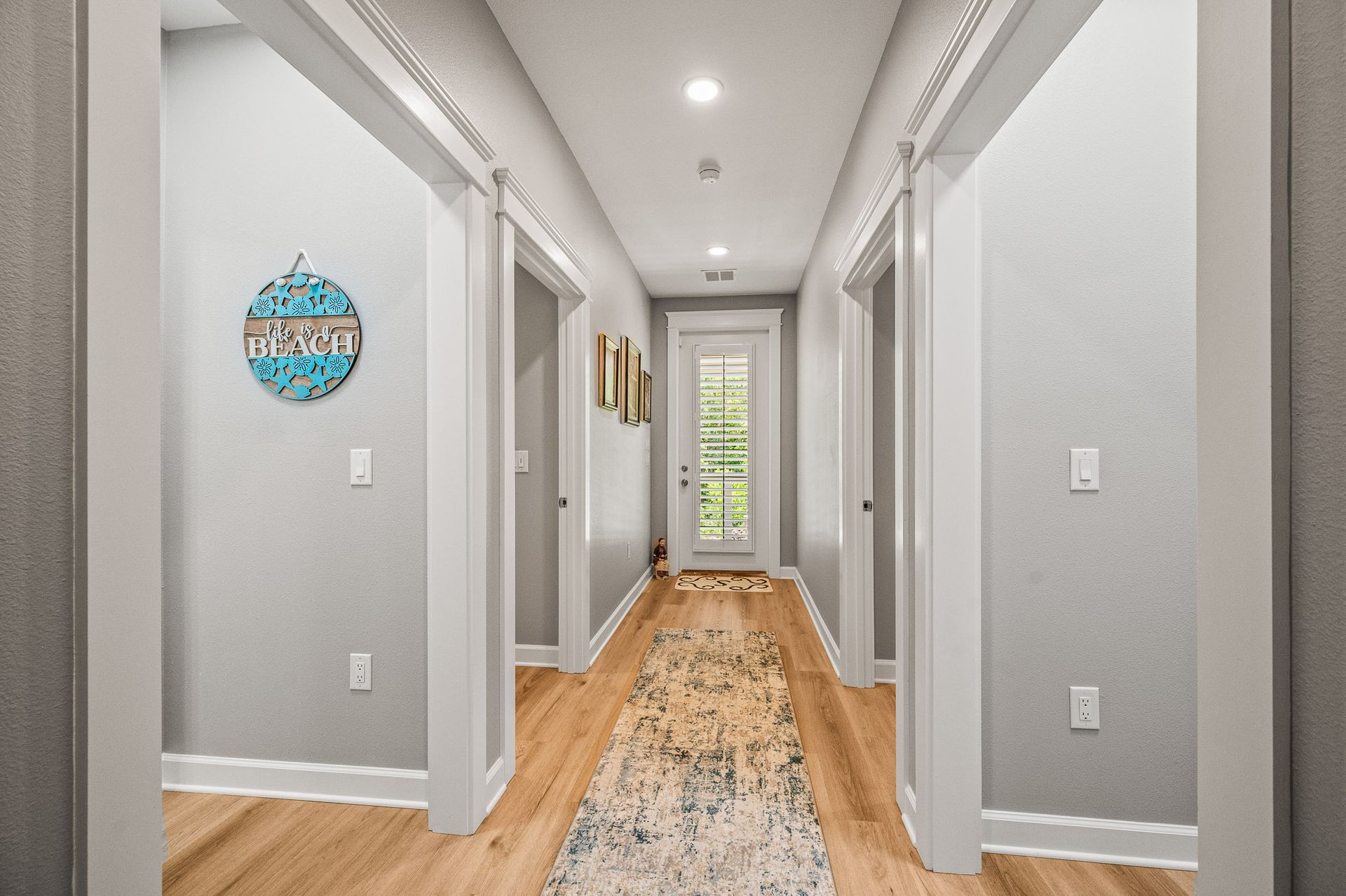 Bright hallway with gray walls, wood floors, recessed lights, and a patterned runner rug.