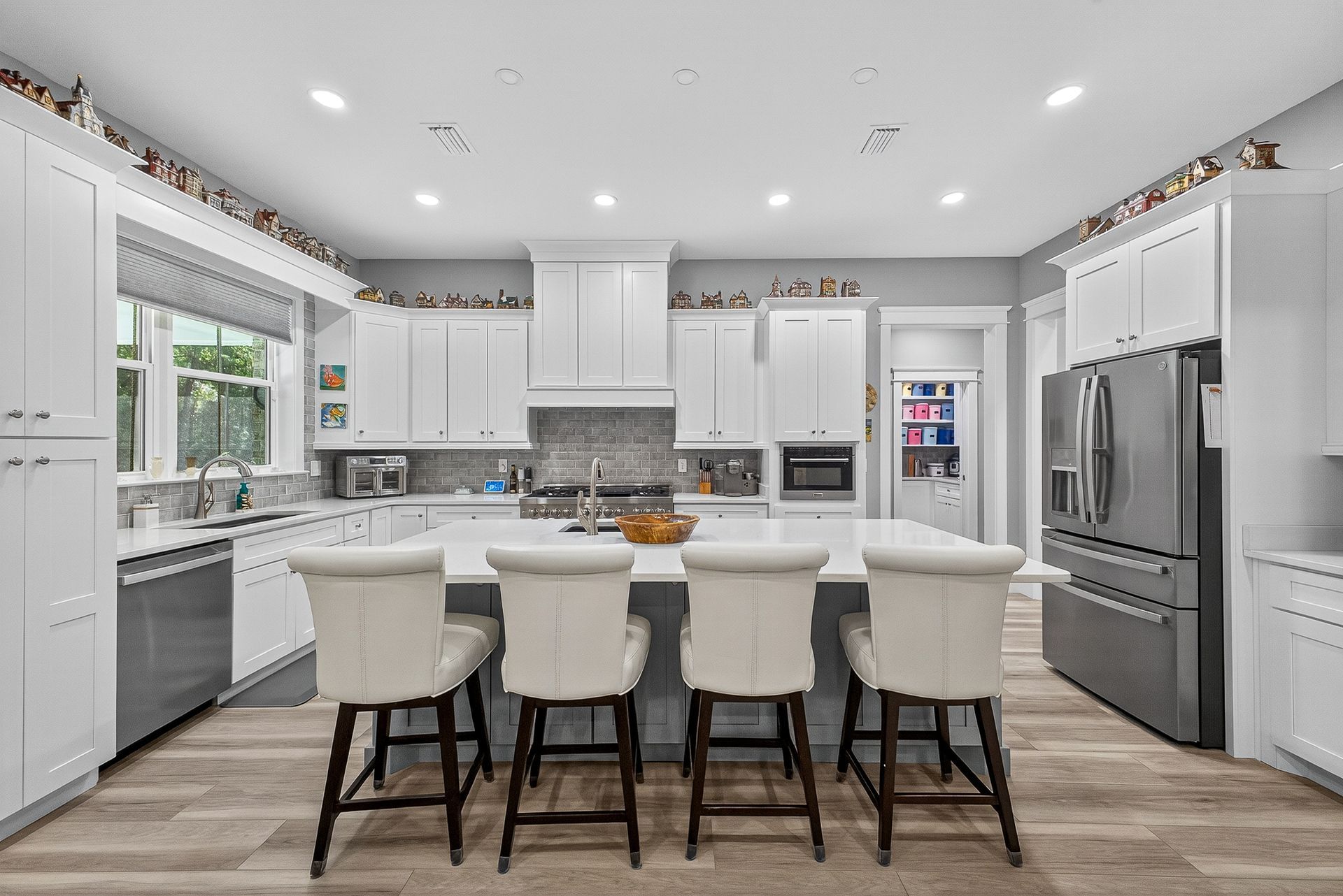 Bright modern white kitchen with island, stools, stainless steel appliances, and wood flooring
