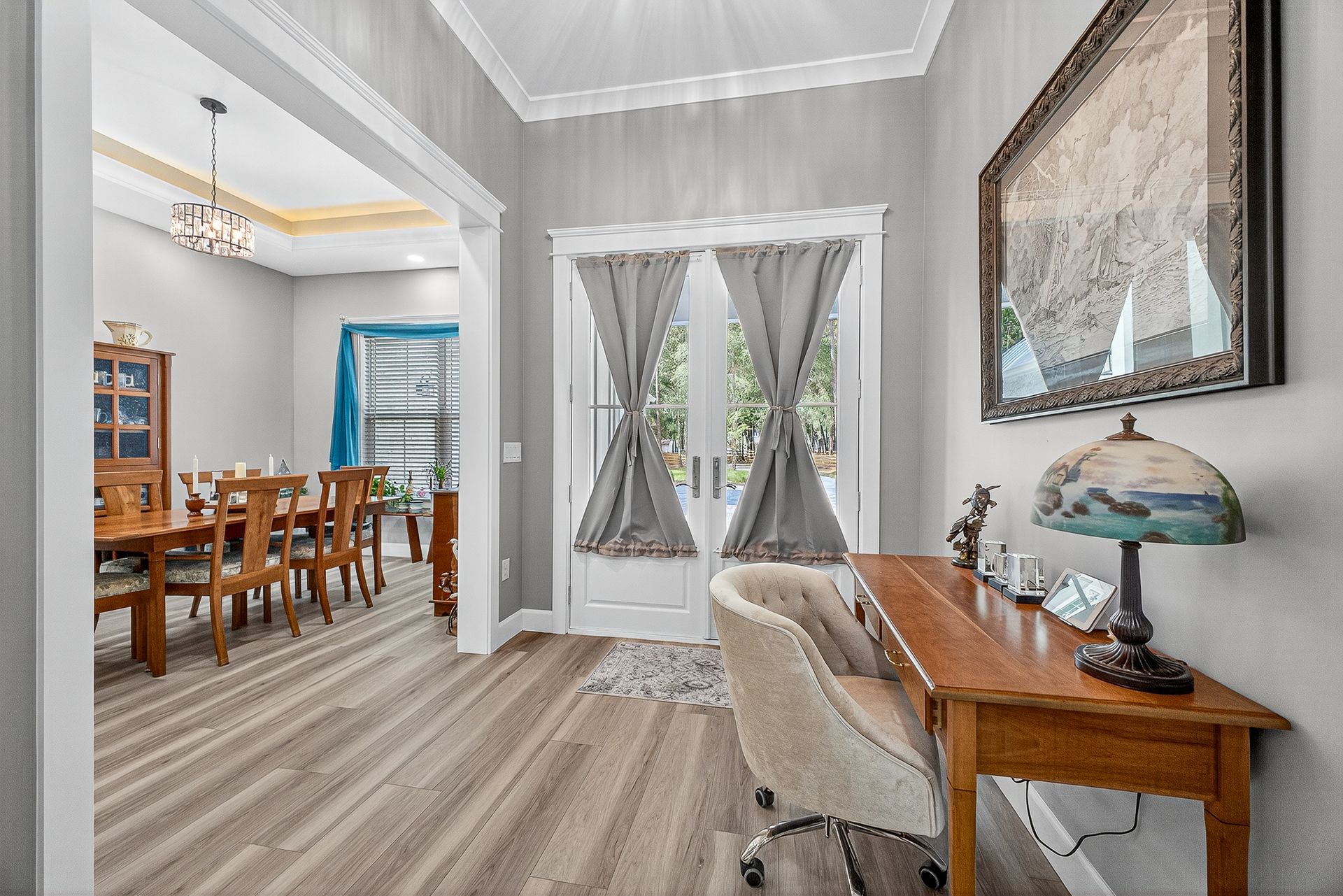 Bright home office with wooden desk, beige chair, striped floor, and dining room visible through archway